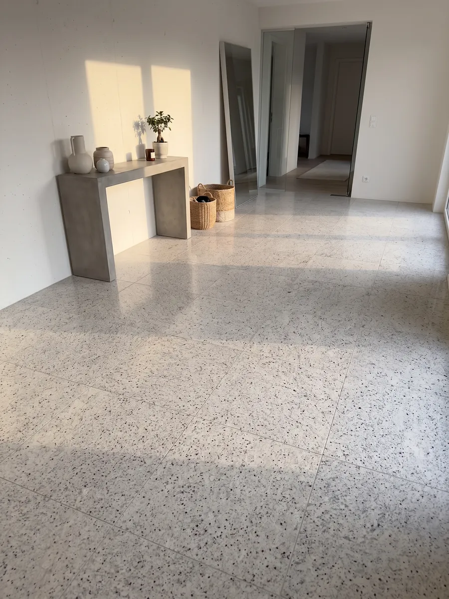 Piso de recibidor en placas grandes de Granito Blanco Dallas con luz natural: blanco cremoso con un moteado fino gris y pequeños puntos burdeos