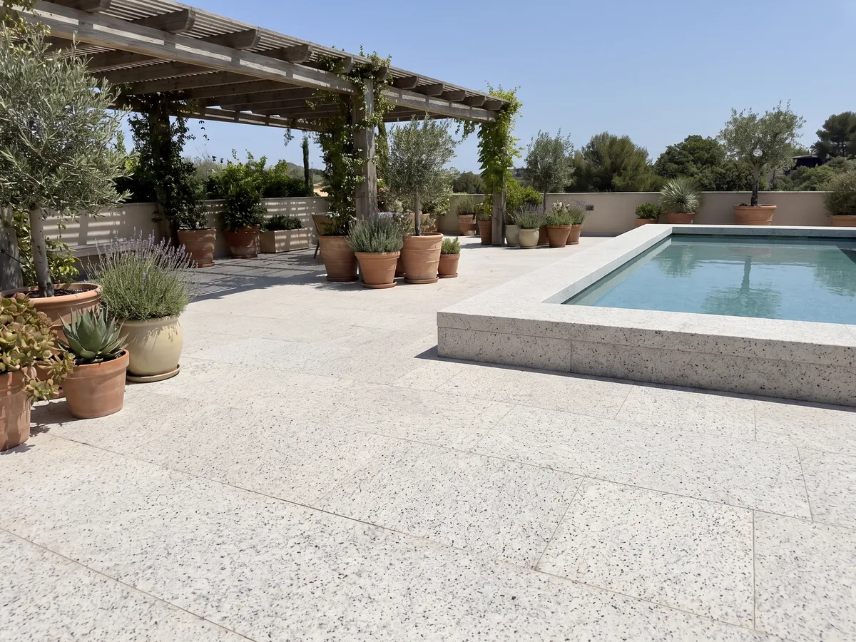 Piso de terraza y borde de piscina en Granito Blanco Dallas con macetas: blanco cremoso con un moteado fino gris y pequeños puntos burdeos