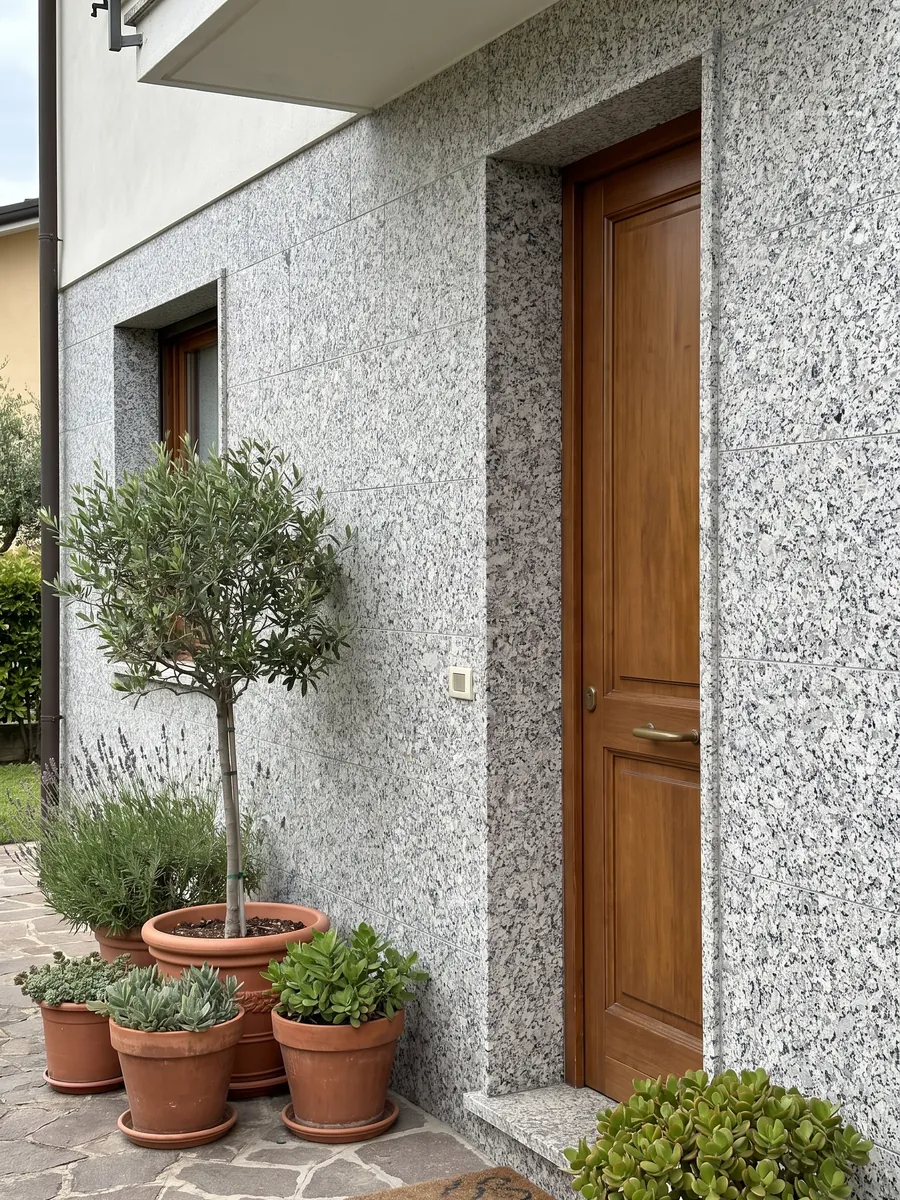 Fachada de casa revestida con granito blanco Sardo Bianco junto a una puerta de madera: blanco de grano grueso con cristales grises y negros