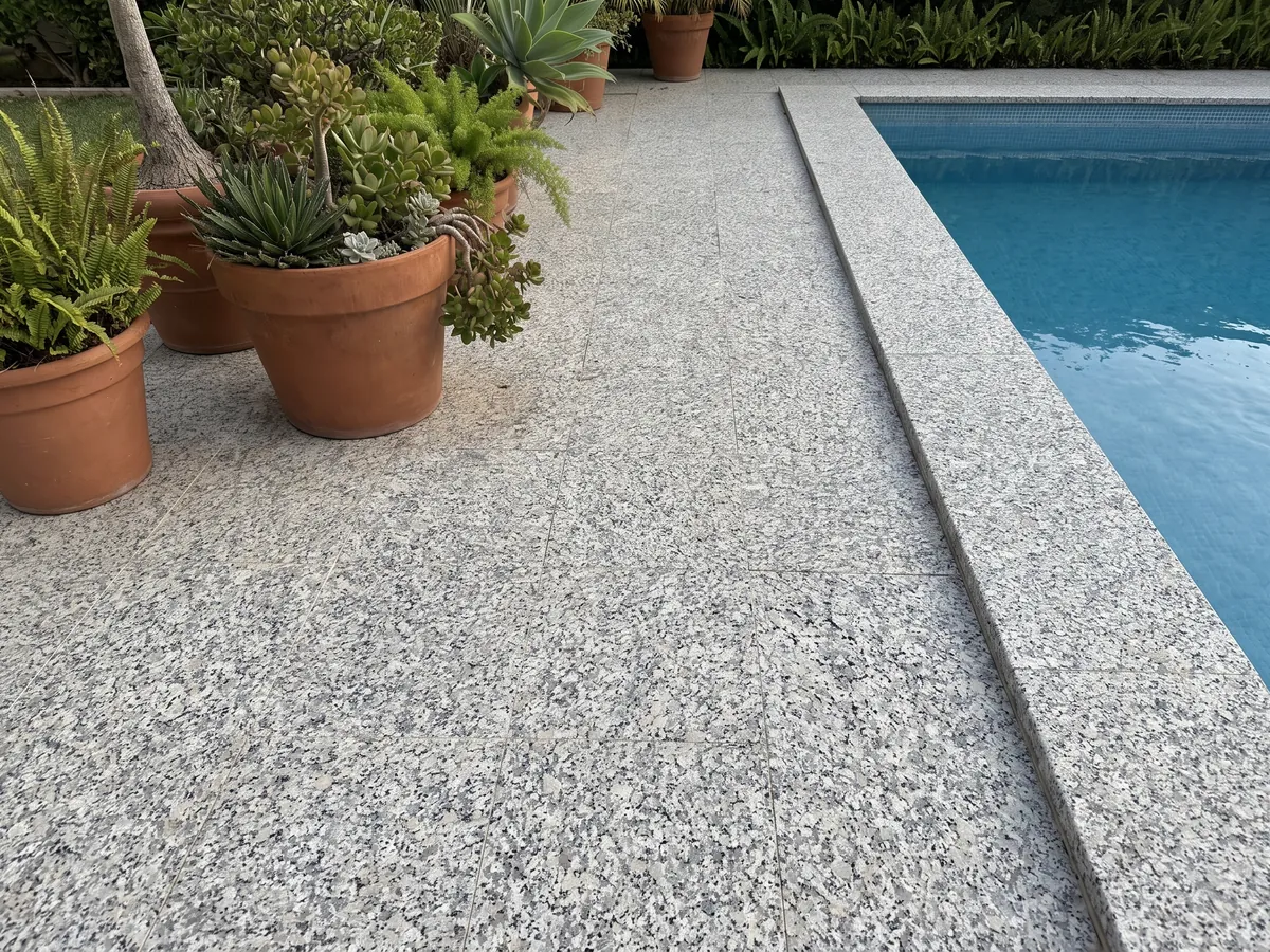 Piso de terraza y borde de piscina en granito blanco Sardo Bianco con macetas: blanco de grano grueso con cristales grises y negros