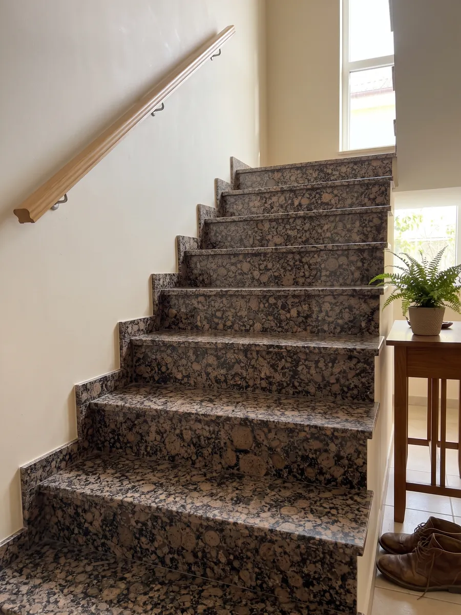 Escalera interior con peldaños de granito café Baltic Brown con pasamanos: granos redondos marrones con anillos sobre fondo moteado negro