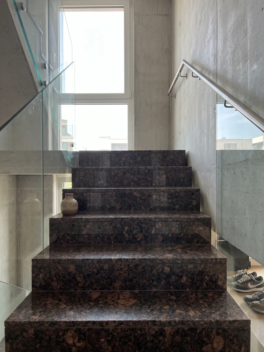 Escalera interior con peldaños de granito café Tan Brown con pasamanos: marrón chocolate con manchas cobrizas grandes y puntos negros