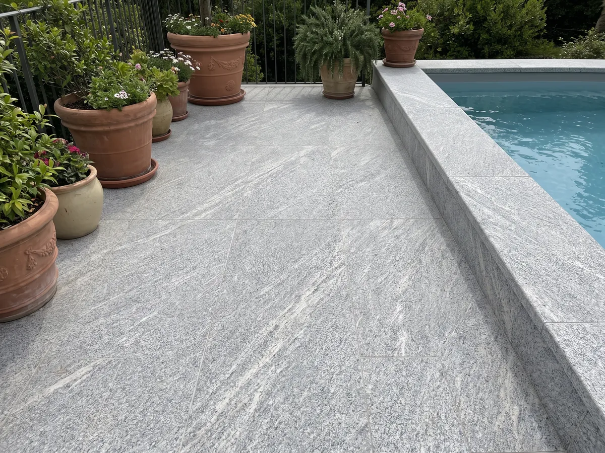 Piso de terraza y borde de piscina en granito gris Beola Grigia con macetas: gris claro granulado con estrías finas en diagonal