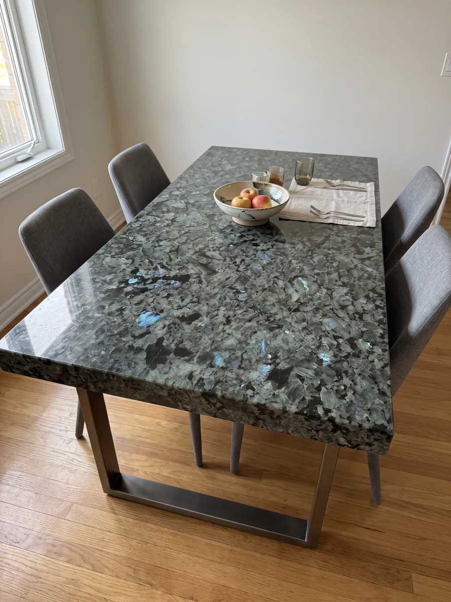 Mesa de comedor con cubierta de granito gris Labradorita sobre base de acero: cristales grandes gris verdosos con destellos azules iridiscentes