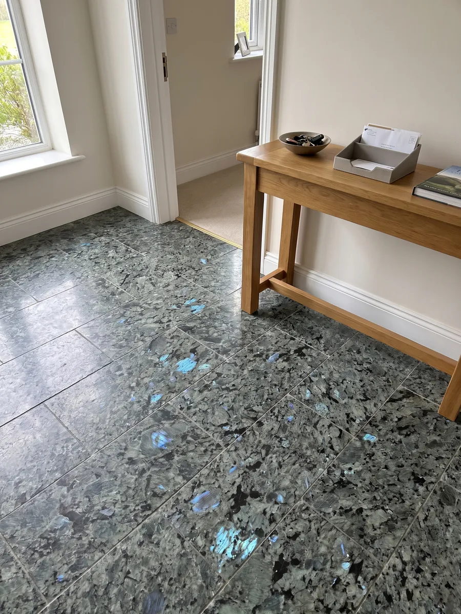 Piso de recibidor en placas grandes de granito gris Labradorita con luz natural: cristales grandes gris verdosos con destellos azules iridiscentes