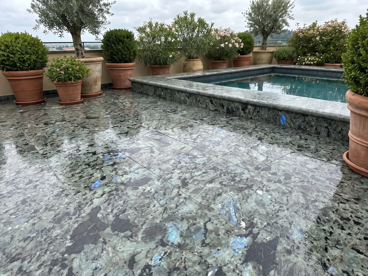 Piso de terraza y borde de piscina en granito gris Labradorita con macetas: cristales grandes gris verdosos con destellos azules iridiscentes