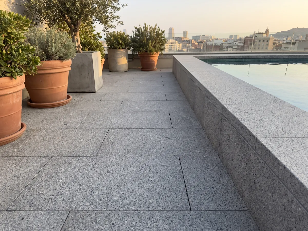 Piso de terraza y borde de piscina en Granito Gris Mara con macetas: gris neutro con grano fino blanco y negro repartido de forma pareja