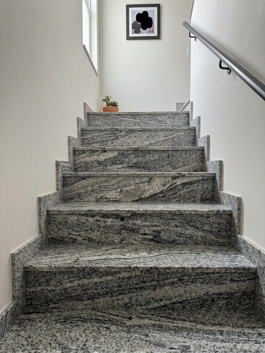 Escalera interior con peldaños de granito gris Piracema White con pasamanos: bandas onduladas gris y blanco con un gran fragmento claro