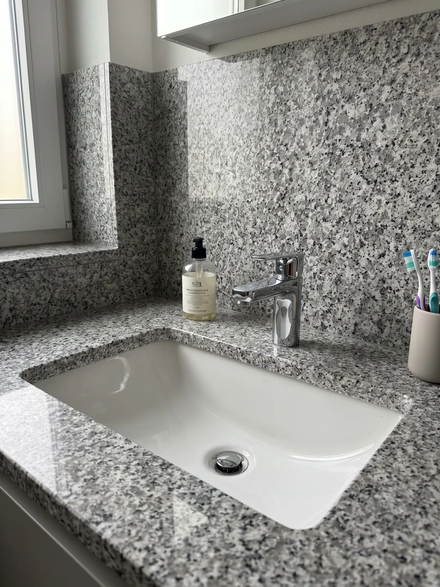 Cubierta de lavabo y pared de baño en granito gris Sardo Grigio con lavamanos blanco y grifería cromada: gris claro sal y pimienta de grano medio