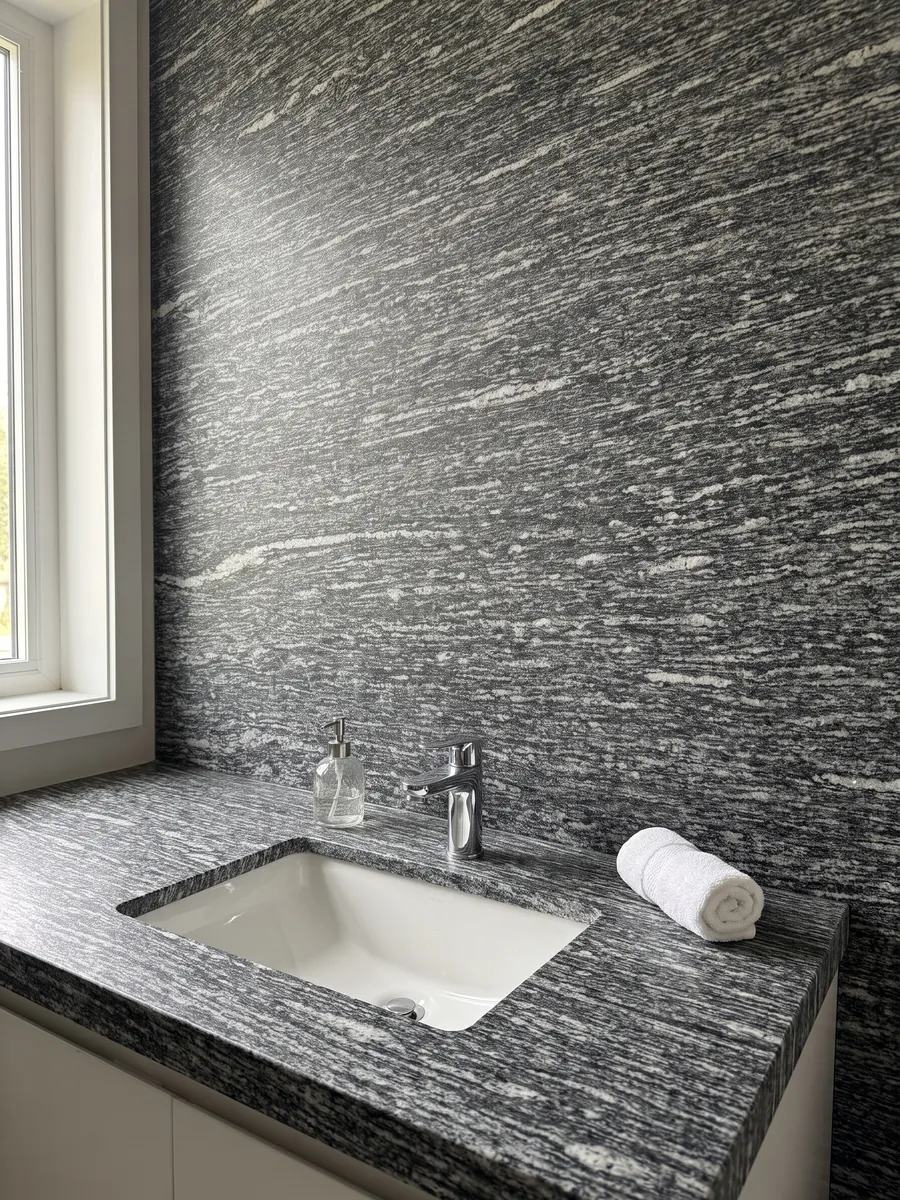 Cubierta de lavabo y pared de baño en granito gris Serizzo con lavamanos blanco y grifería cromada: gris oscuro con trazos blancos alargados horizontales
