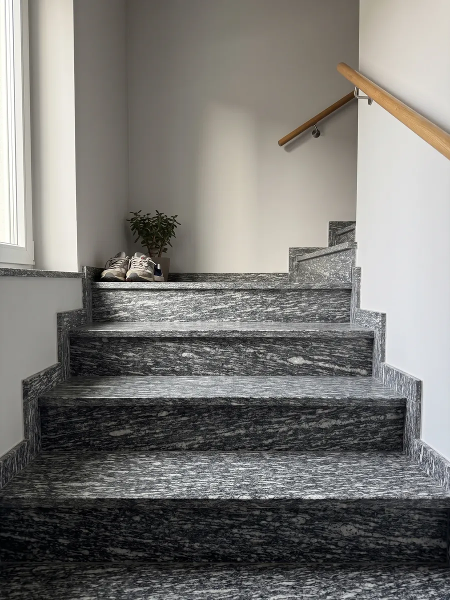 Escalera interior con peldaños de granito gris Serizzo con pasamanos: gris oscuro con trazos blancos alargados horizontales