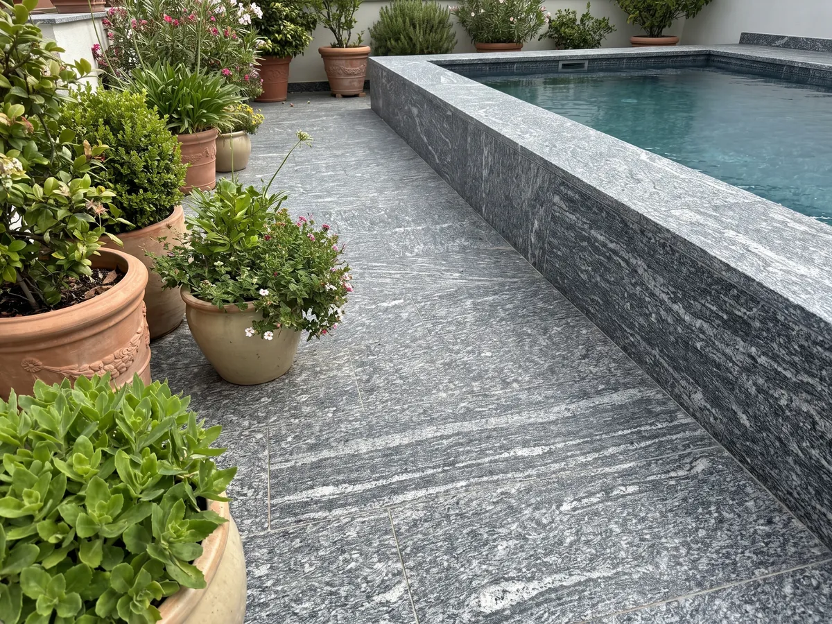 Piso de terraza y borde de piscina en granito gris Serizzo con macetas: gris oscuro con trazos blancos alargados horizontales