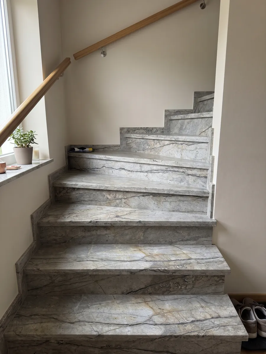 Escalera interior con peldaños de granito gris Silver Roots con pasamanos: gris topo con vetas oscuras horizontales y aspecto de piedra natural