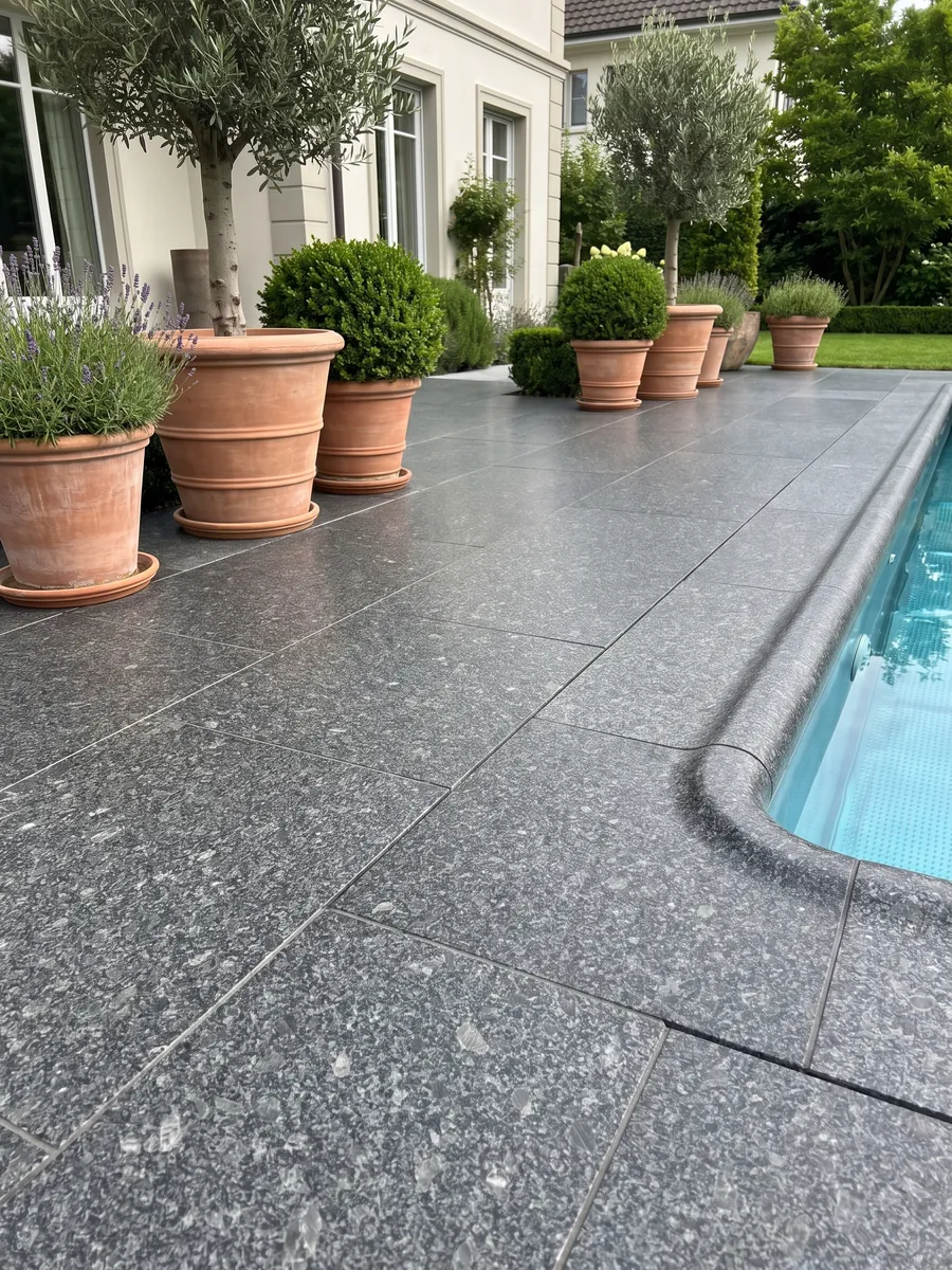 Piso de terraza y borde de piscina en granito gris Steel Grey con macetas: grano medio gris acero sobre fondo casi negro, con pequeñas áreas grises más claras repartidas