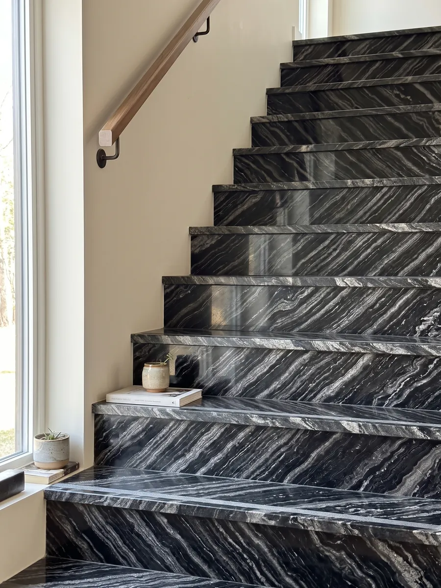 Escalera interior con peldaños de granito negro Agata Black con pasamanos: negro con bandas onduladas gris plata paralelas en diagonal