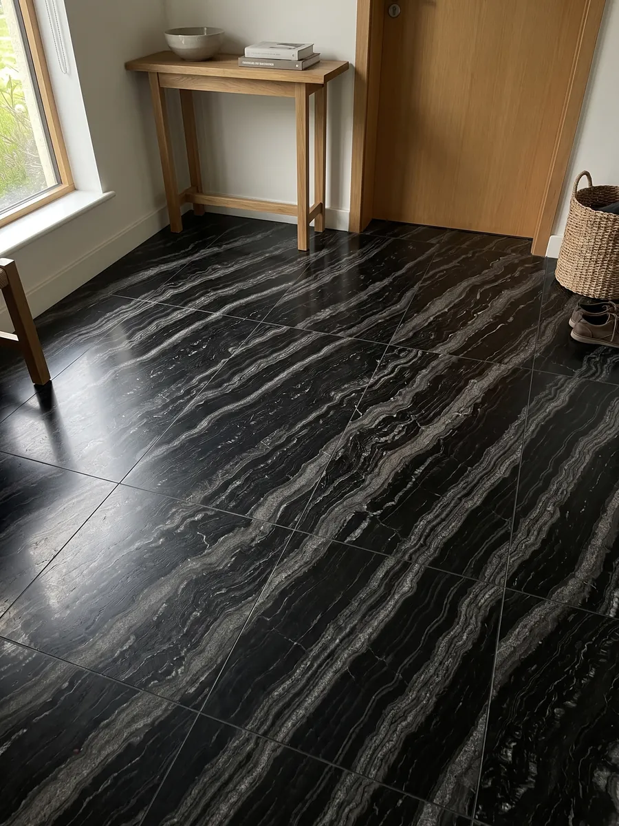 Piso de recibidor en placas grandes de granito negro Agata Black con luz natural: negro con bandas onduladas gris plata paralelas en diagonal