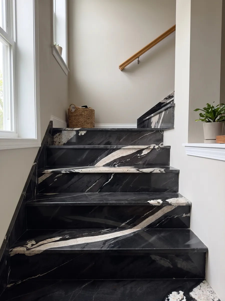 Escalera interior con peldaños de granito negro Copacabana con pasamanos: negro con una banda crema ondulada que cruza en diagonal