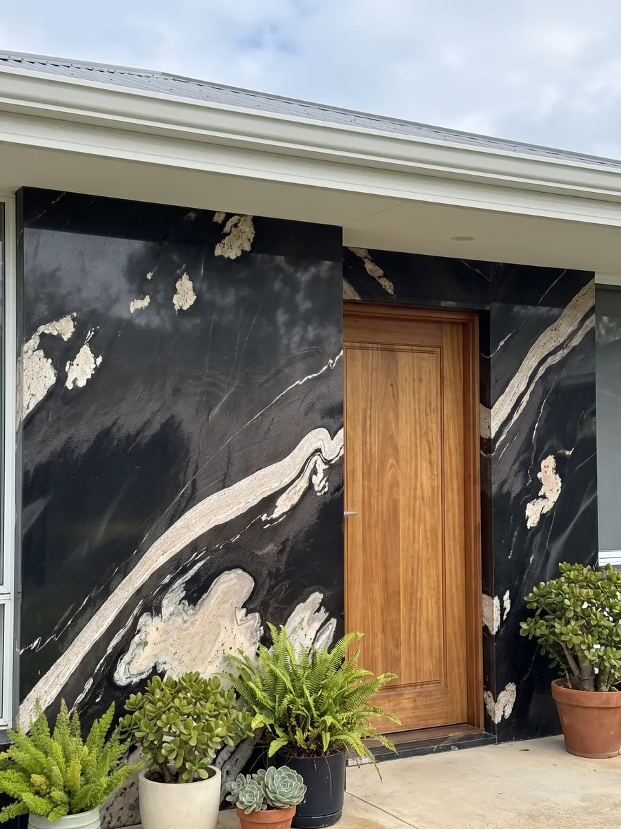Fachada de casa revestida con granito negro Copacabana junto a una puerta de madera: negro con una banda crema ondulada que cruza en diagonal