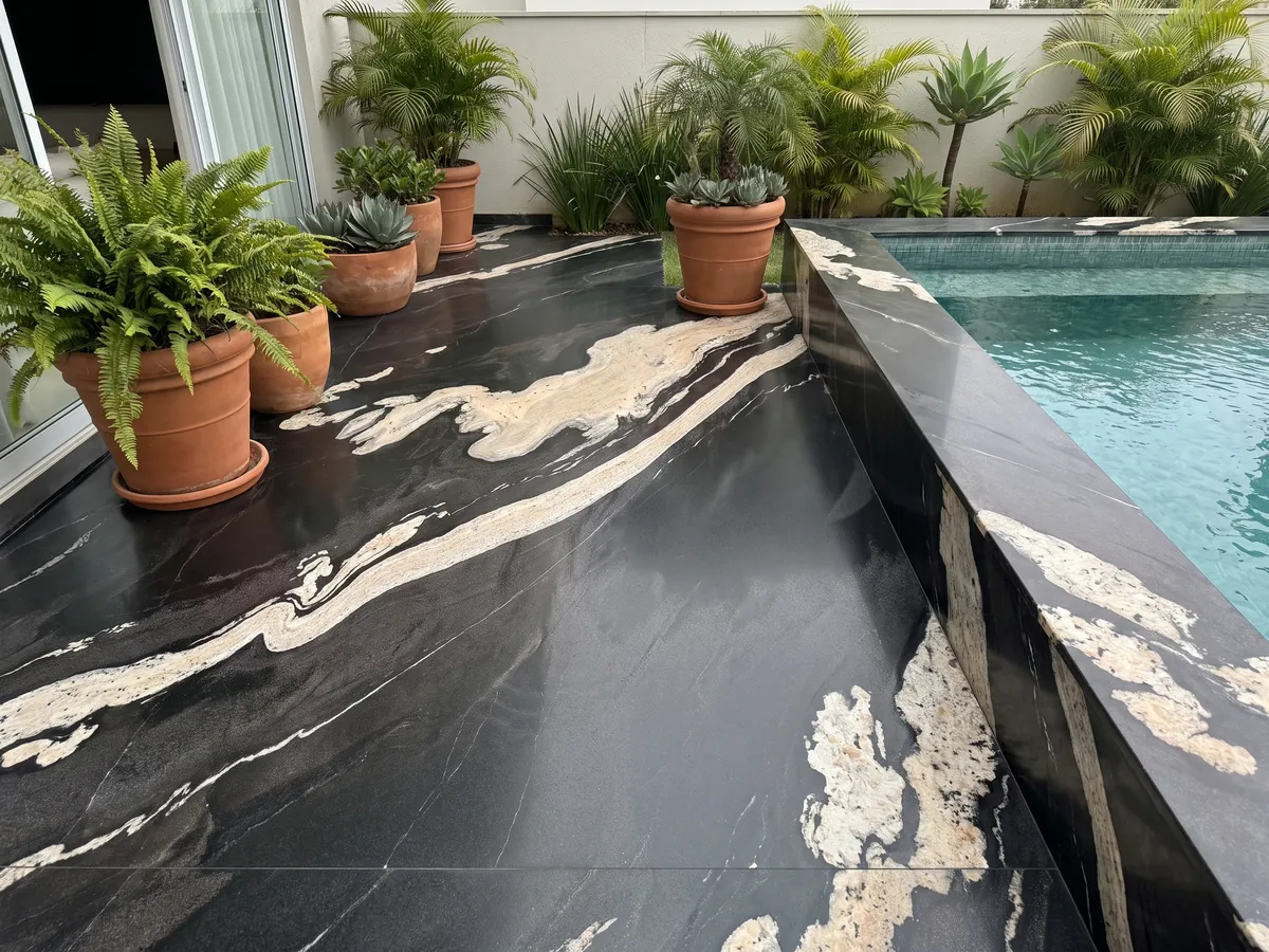 Piso de terraza y borde de piscina en granito negro Copacabana con macetas: negro con una banda crema ondulada que cruza en diagonal