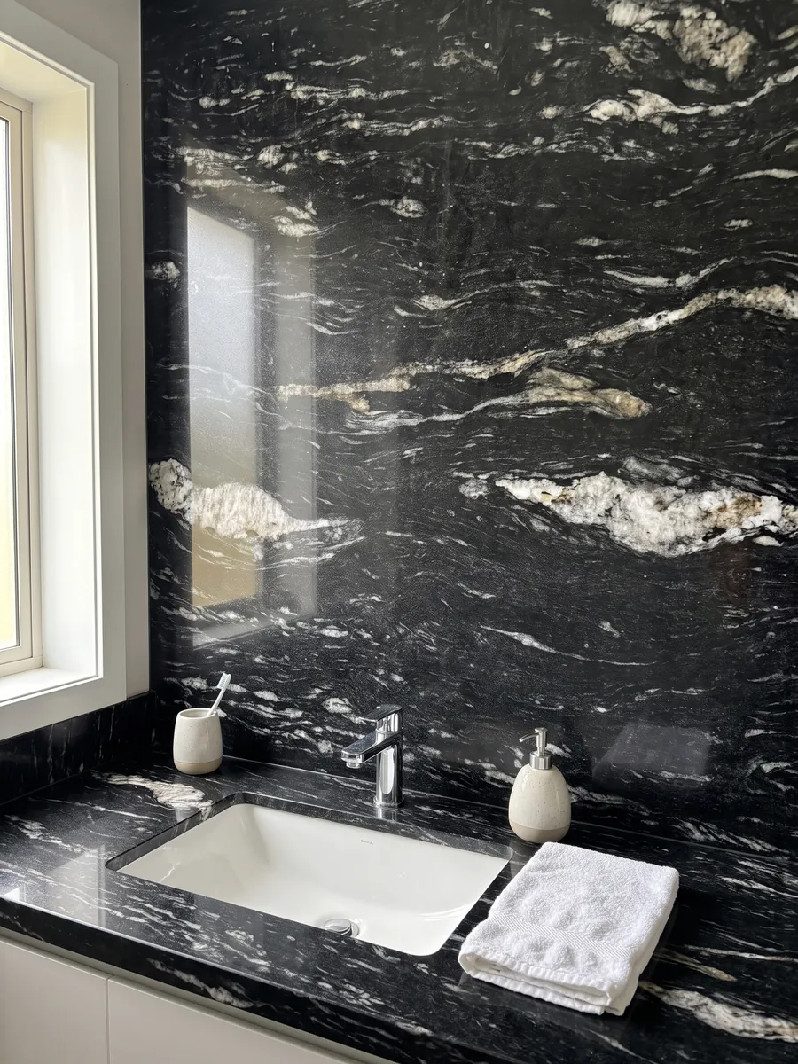 Cubierta de lavabo y pared de baño en granito negro Cosmic Black con lavamanos blanco y grifería cromada: negro con trazos blancos ondulados horizontales