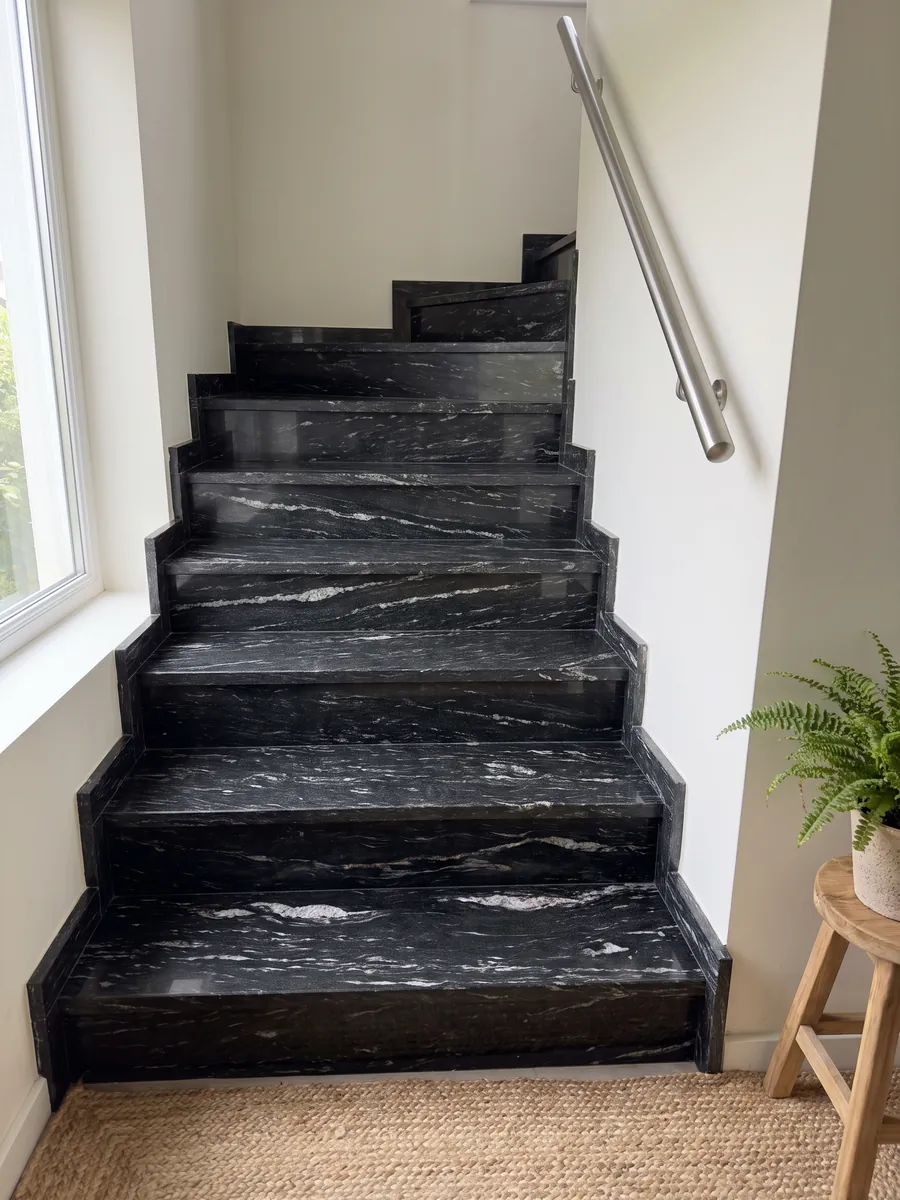 Escalera interior con peldaños de granito negro Cosmic Black con pasamanos: negro con trazos blancos ondulados horizontales
