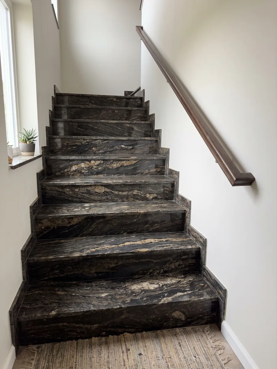 Escalera interior con peldaños de granito negro Cosmic Gold con pasamanos: negro con zonas doradas y bronce en ondas horizontales
