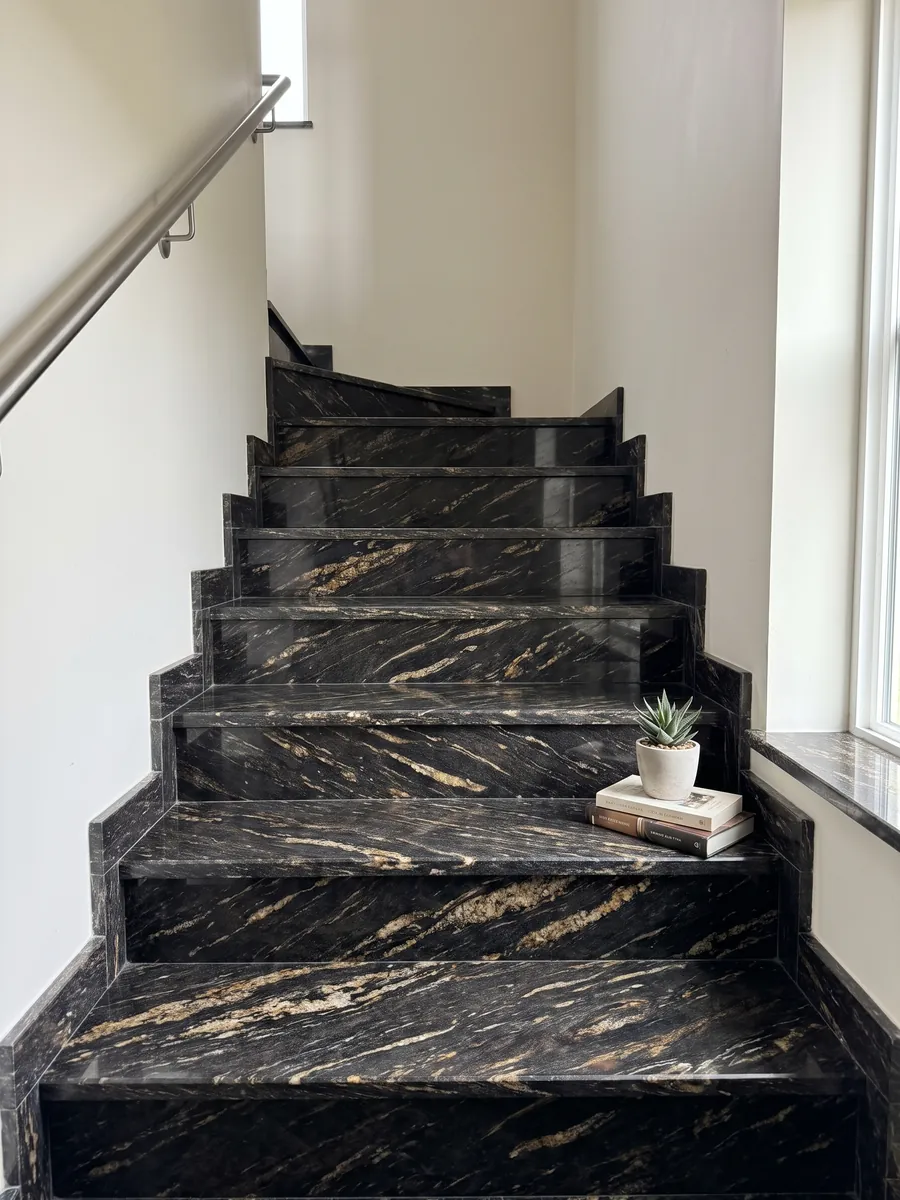 Escalera interior con peldaños de granito negro Matrix con pasamanos: negro con trazos dorados alargados en diagonal