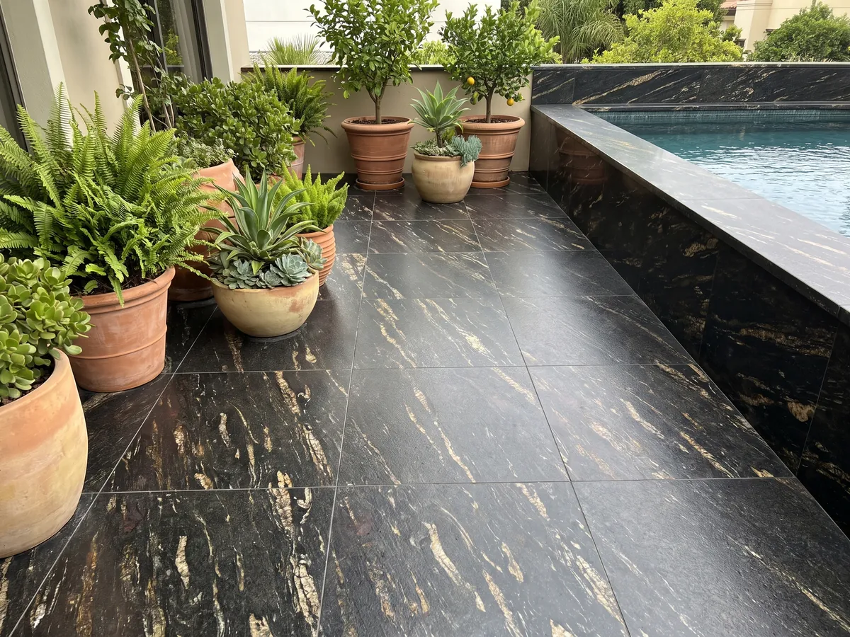 Piso de terraza y borde de piscina en granito negro Matrix con macetas: negro con trazos dorados alargados en diagonal