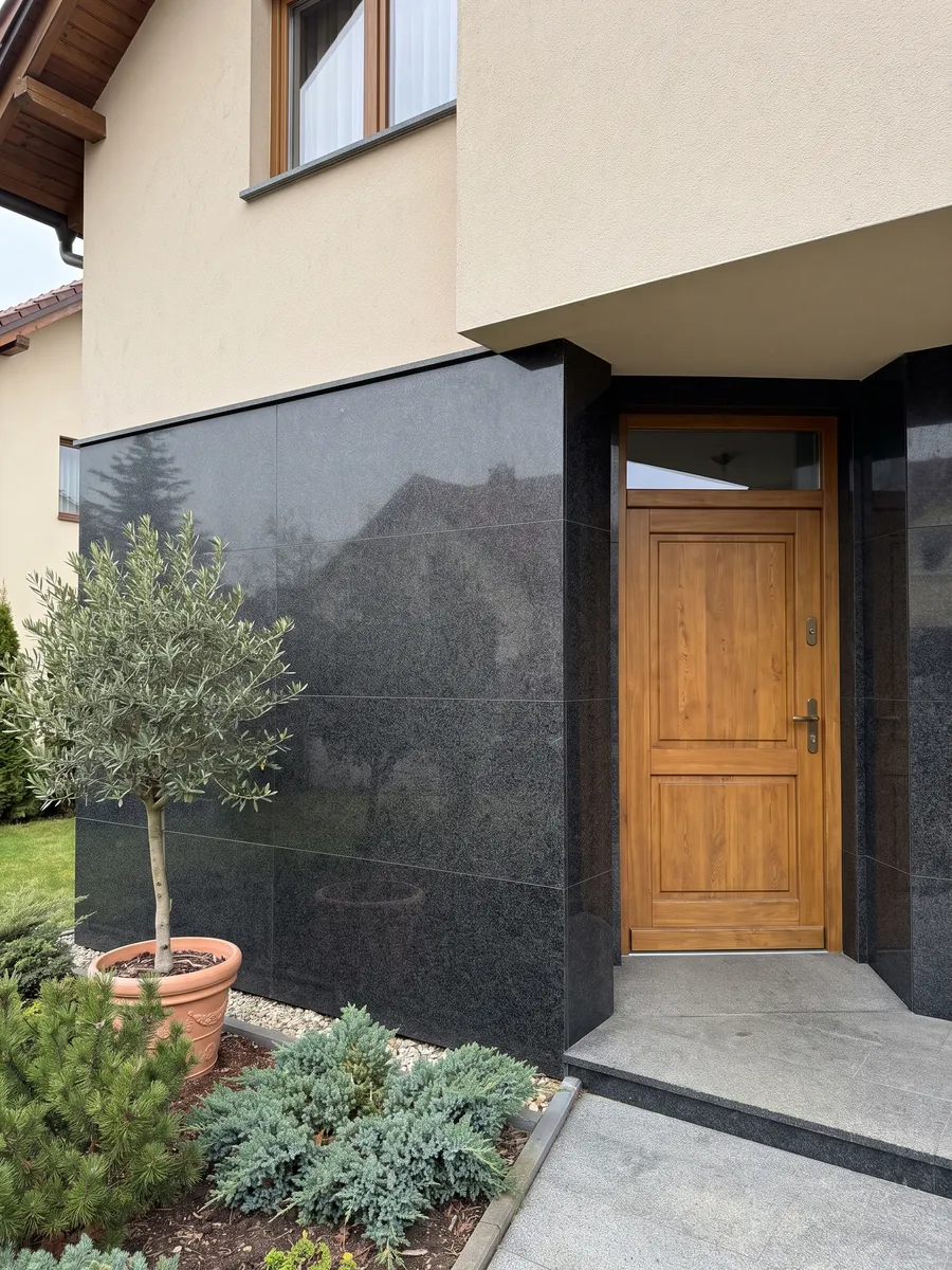 Fachada de casa revestida con granito negro Nero Africa junto a una puerta de madera: negro de grano fino uniforme con leve punteado gris