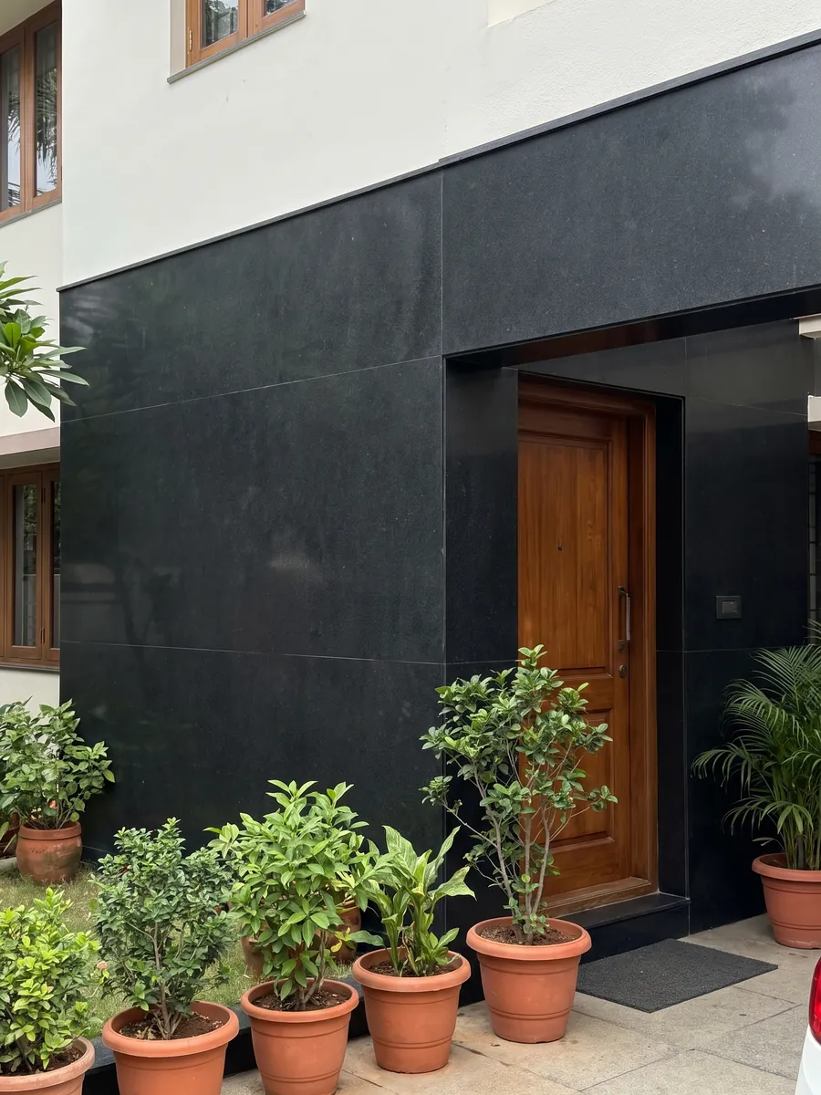 Fachada de casa revestida con granito negro Nero Assoluto junto a una puerta de madera: negro uniforme sin dibujo