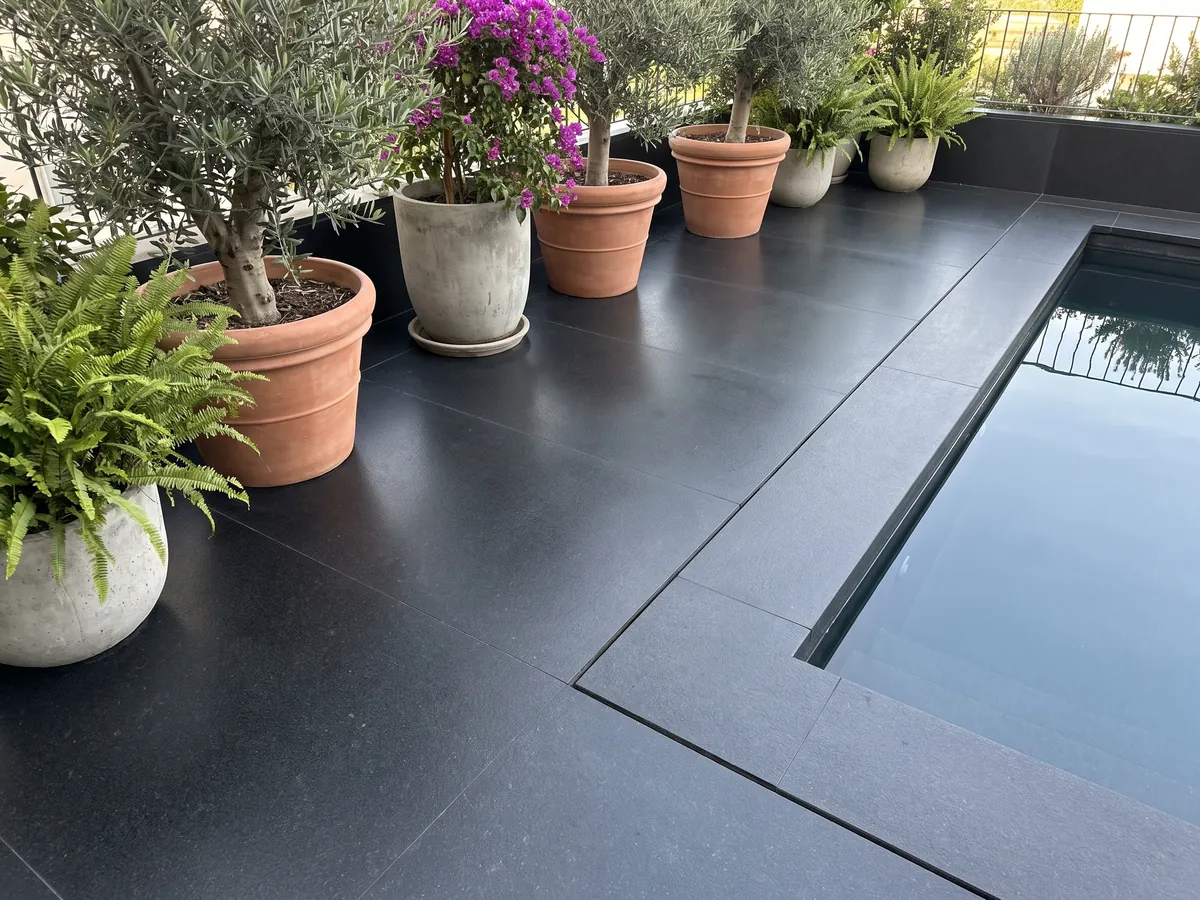 Piso de terraza y borde de piscina en granito negro Nero Assoluto con macetas: negro uniforme sin dibujo