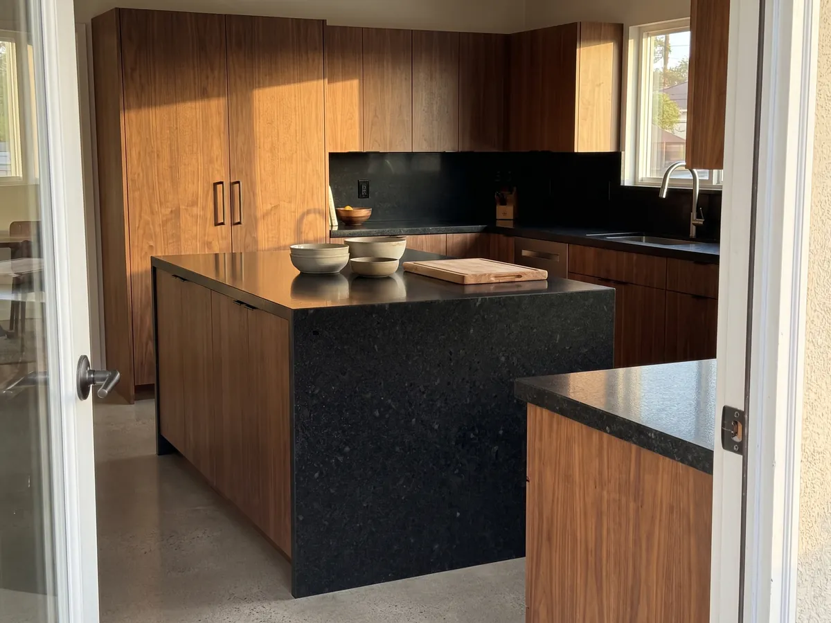 Isla de cocina con cubierta de Granito Negro San Gabriel y canto recto en una cocina con luz natural: negro profundo de grano medio con motas gris oscuro que se ven de cerca