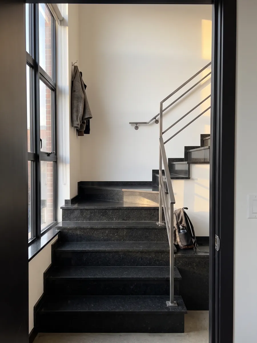 Escalera interior con peldaños de Granito Negro San Gabriel con pasamanos: negro profundo de grano medio con motas gris oscuro que se ven de cerca