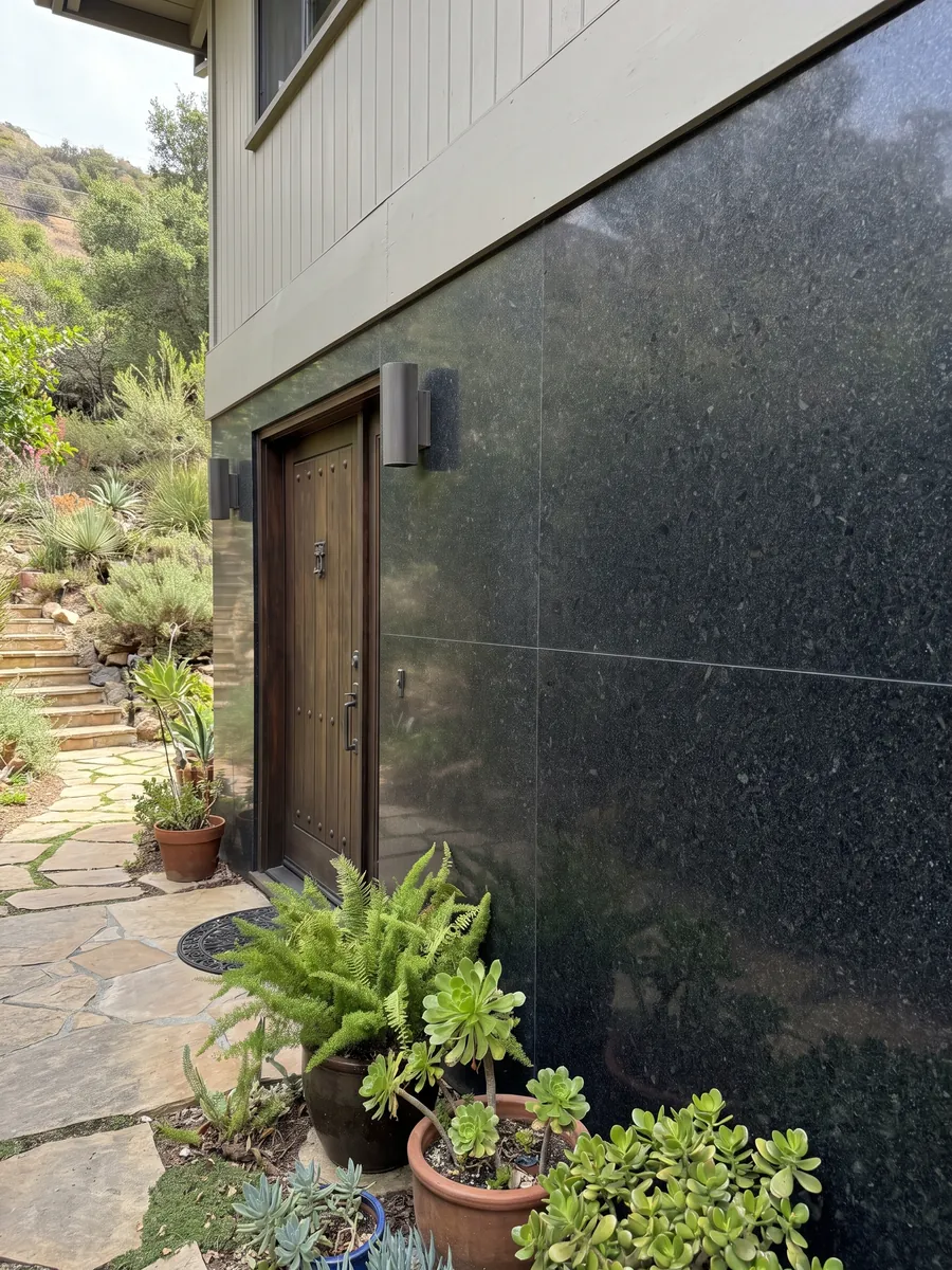 Fachada de casa revestida con Granito Negro San Gabriel junto a una puerta de madera: negro profundo de grano medio con motas gris oscuro que se ven de cerca