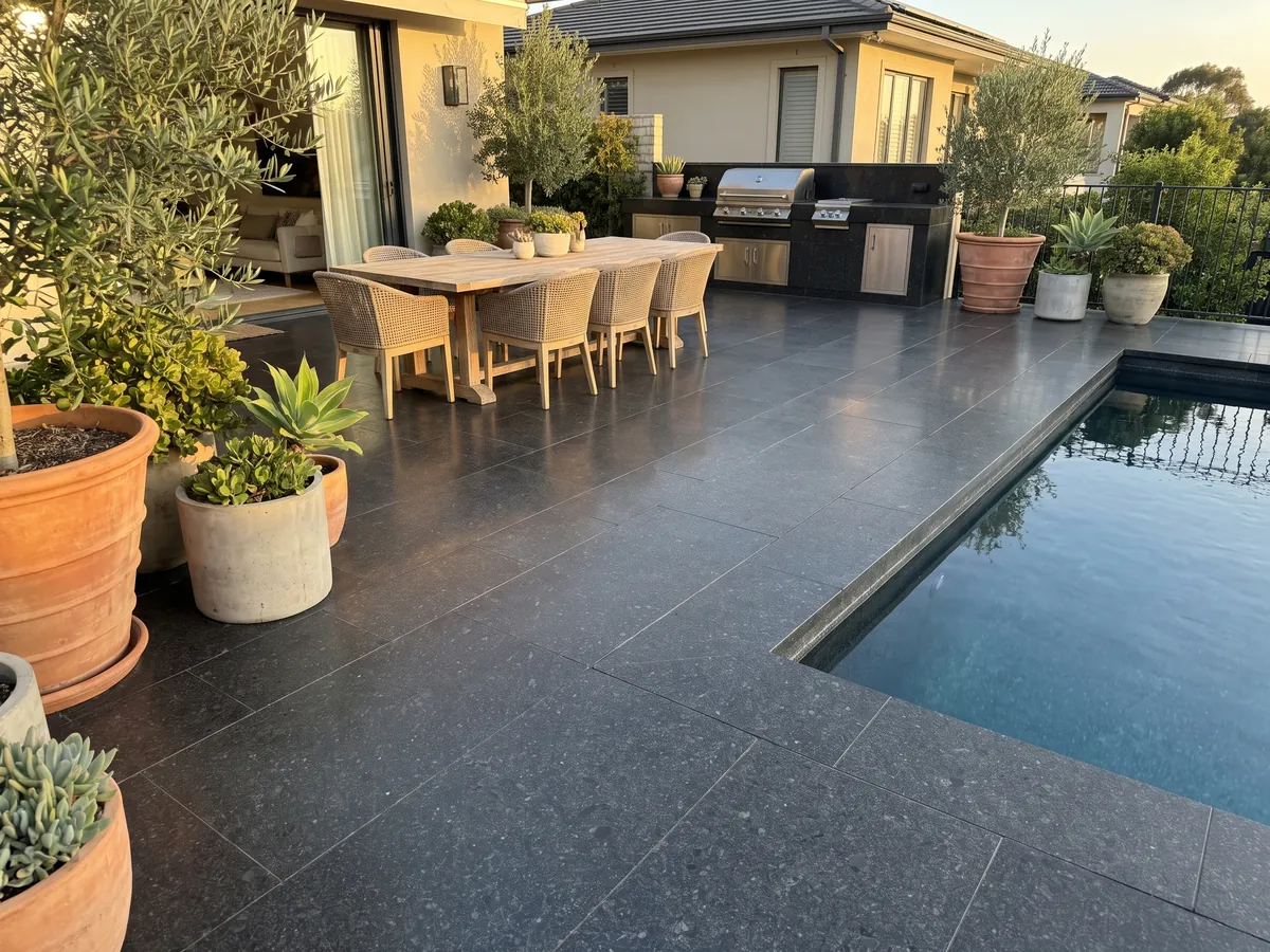 Piso de terraza y borde de piscina en Granito Negro San Gabriel con macetas: negro profundo de grano medio con motas gris oscuro que se ven de cerca