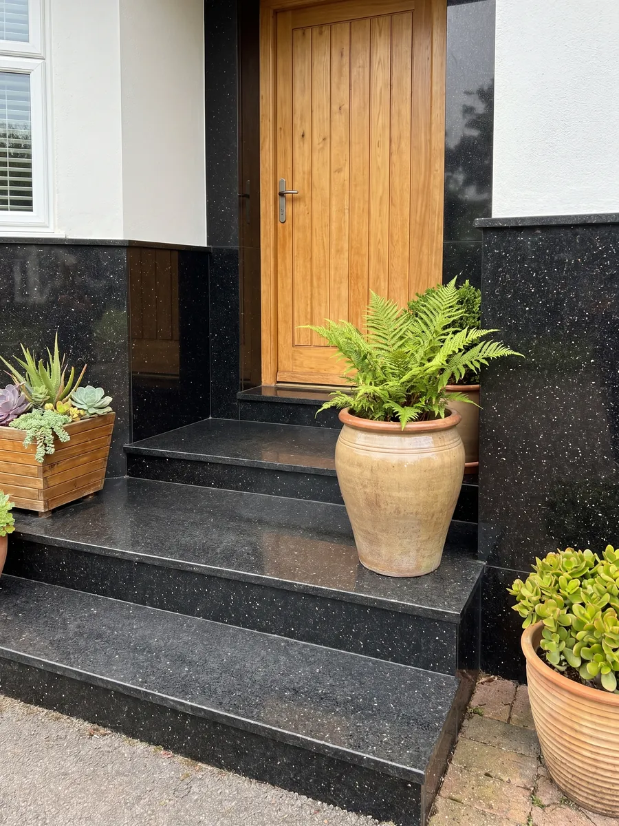 Fachada de casa revestida con granito negro Star Galaxy junto a una puerta de madera: negro con pequeños puntos dorados que brillan