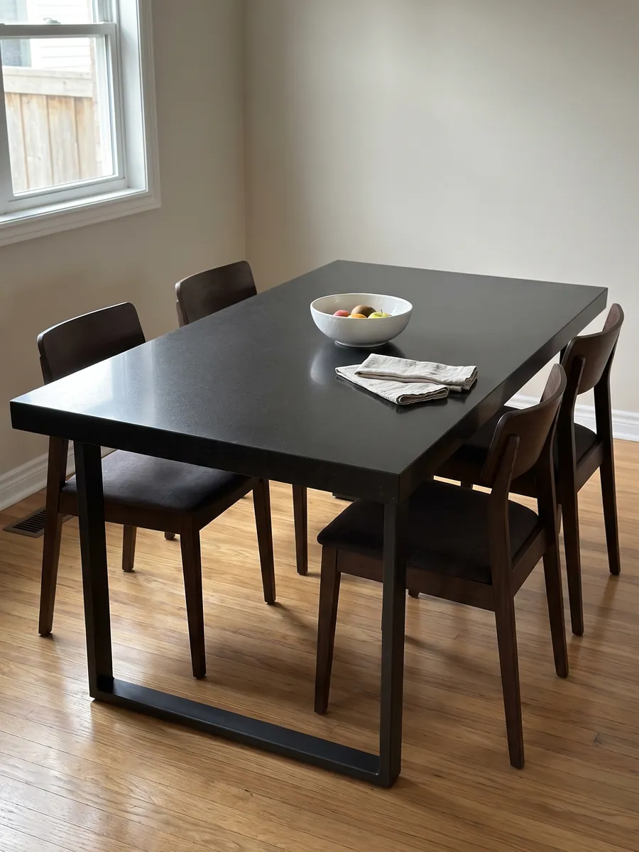 Mesa de comedor con cubierta de granito negro Titanium Black sobre base de acero: negro casi liso y homogéneo, con un grano finísimo que solo se nota de cerca
