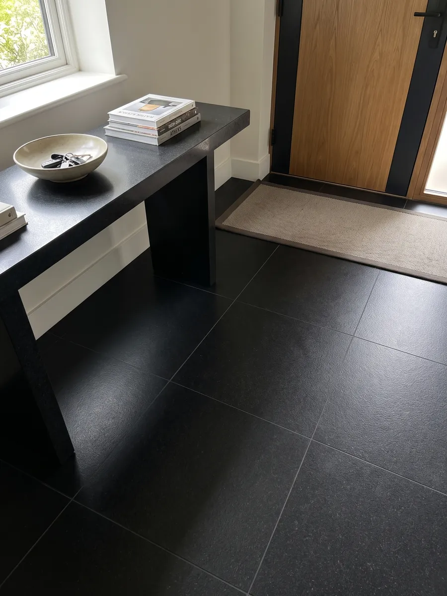Piso de recibidor en placas grandes de granito negro Titanium Black con luz natural: negro casi liso y homogéneo, con un grano finísimo que solo se nota de cerca