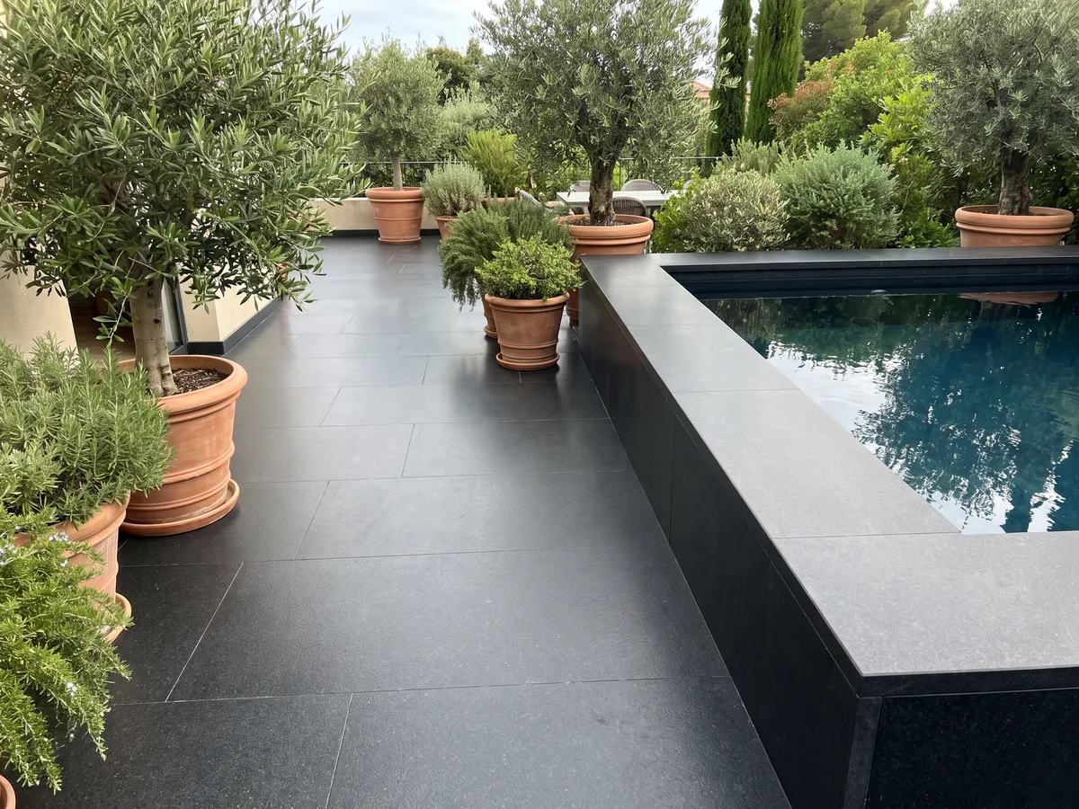 Piso de terraza y borde de piscina en granito negro Titanium Black con macetas: negro casi liso y homogéneo, con un grano finísimo que solo se nota de cerca