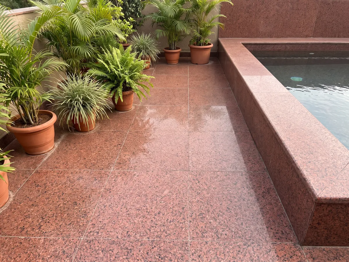 Piso de terraza y borde de piscina en granito rojo Balmoral Red con macetas: rojo intenso granulado con puntos negros repartidos