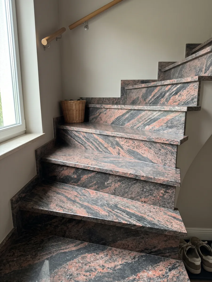 Escalera interior con peldaños de granito rojo Indian Aurora con pasamanos: ondas de color coral y gris oscuro en diagonal