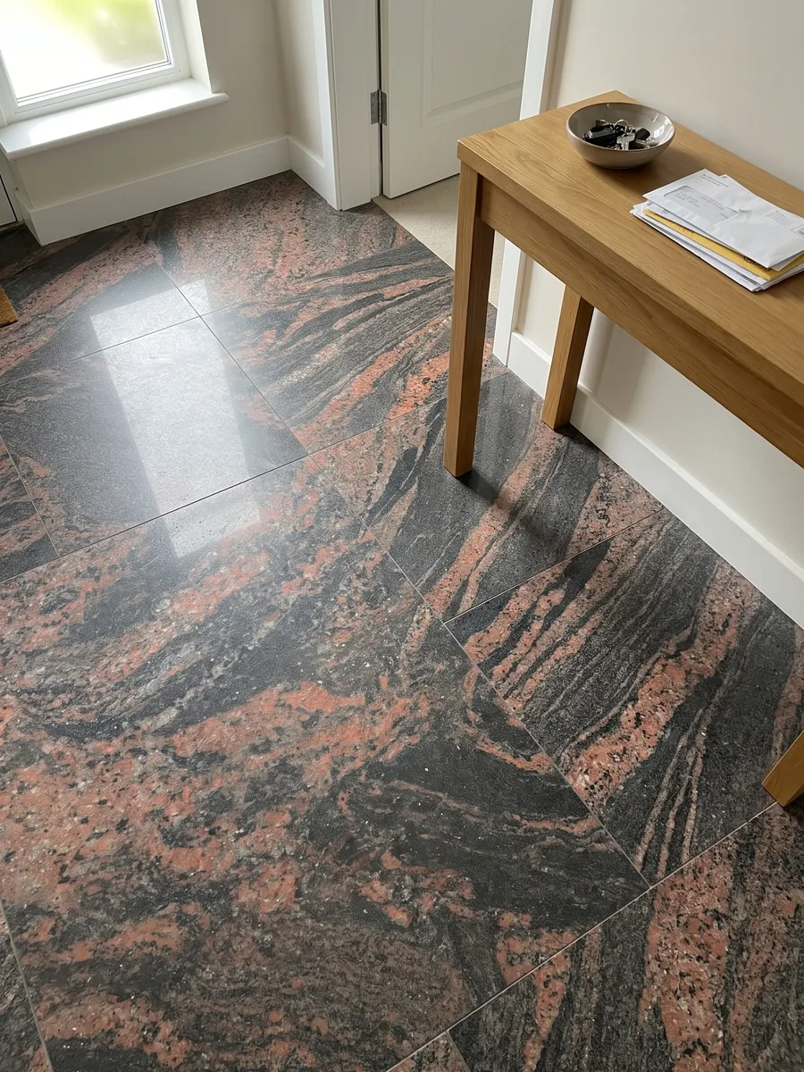 Piso de recibidor en placas grandes de granito rojo Indian Aurora con luz natural: ondas de color coral y gris oscuro en diagonal