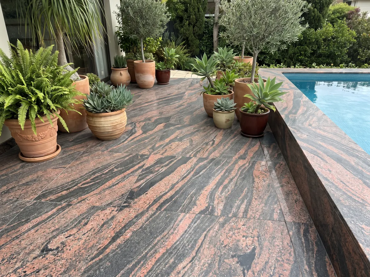 Piso de terraza y borde de piscina en granito rojo Indian Aurora con macetas: ondas de color coral y gris oscuro en diagonal