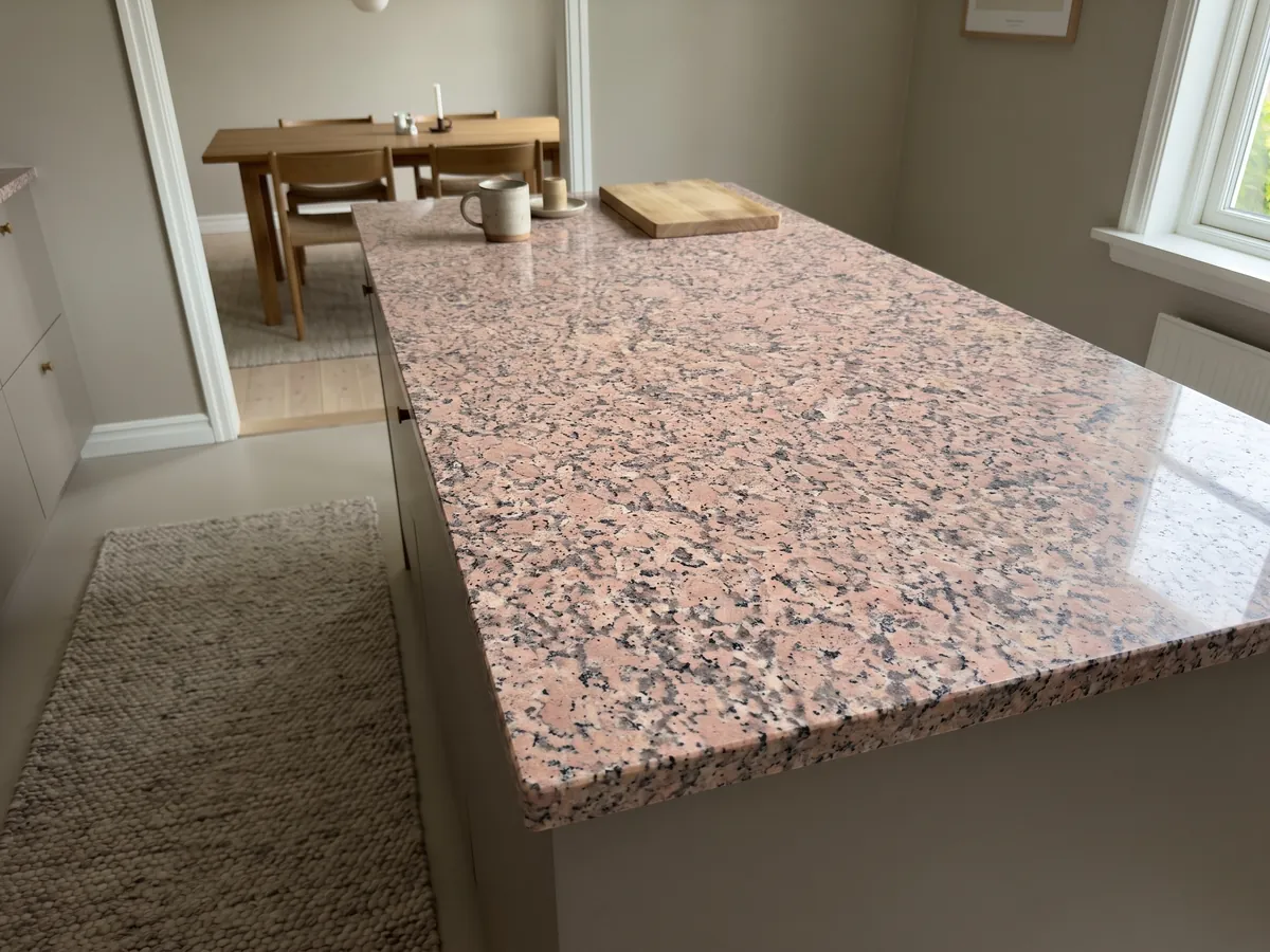 Isla de cocina con cubierta de Granito Rosa de Salto y canto recto en una cocina con luz natural: rosado moteado con puntos gris oscuro y blancos