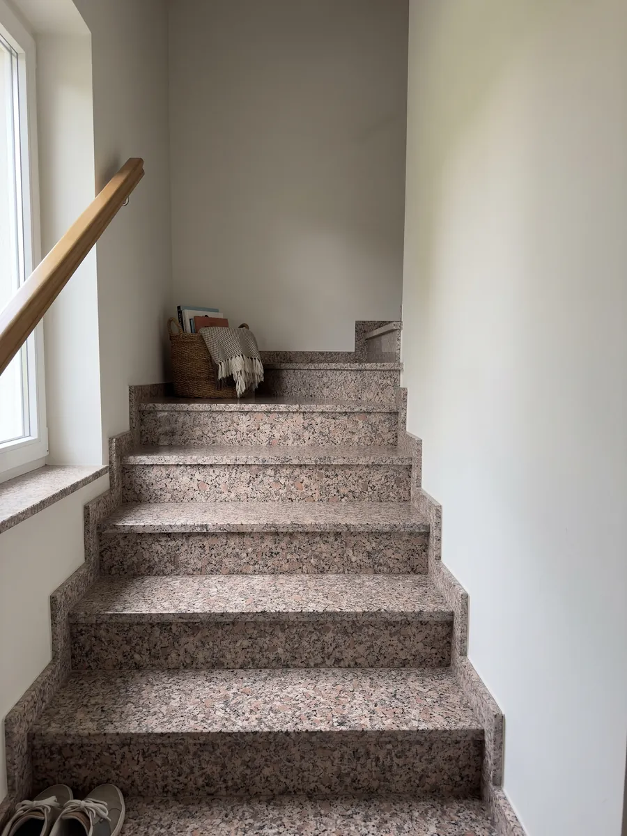 Escalera interior con peldaños de granito rosa Limbara con pasamanos: grano rosado marrón con cristales blancos y negros