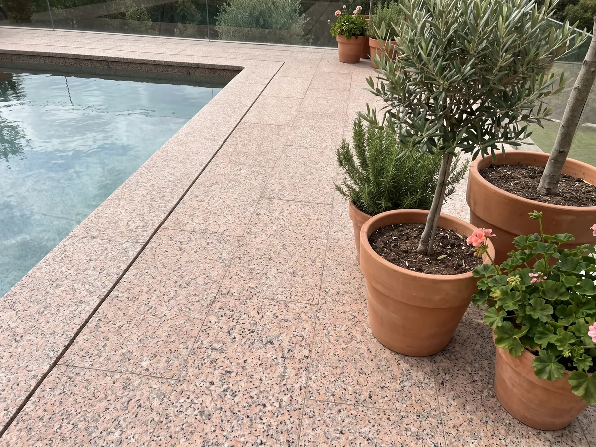 Piso de terraza y borde de piscina en Granito Rosa Porriño con macetas: rosa salmón granulado con puntos negros