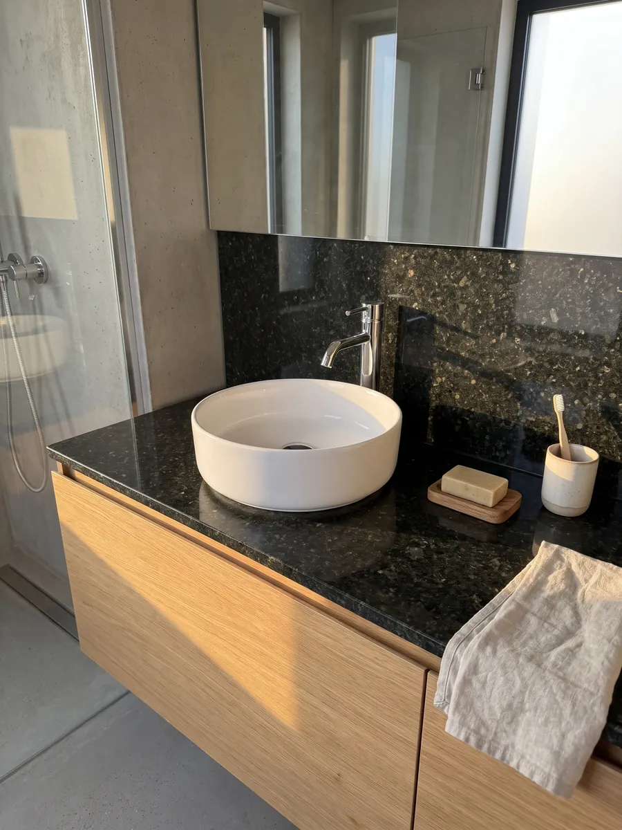 Cubierta de lavabo y pared de baño en Granito Verde Ubatuba con lavamanos blanco y grifería cromada: verde casi negro con destellos de verde claro y dorado