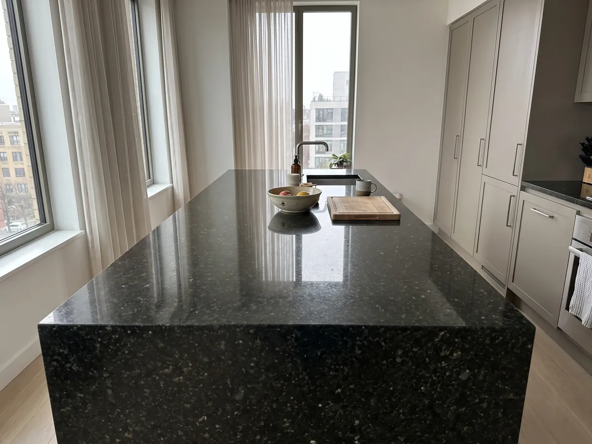 Isla de cocina con cubierta de Granito Verde Ubatuba y canto recto en una cocina con luz natural: verde casi negro con destellos de verde claro y dorado