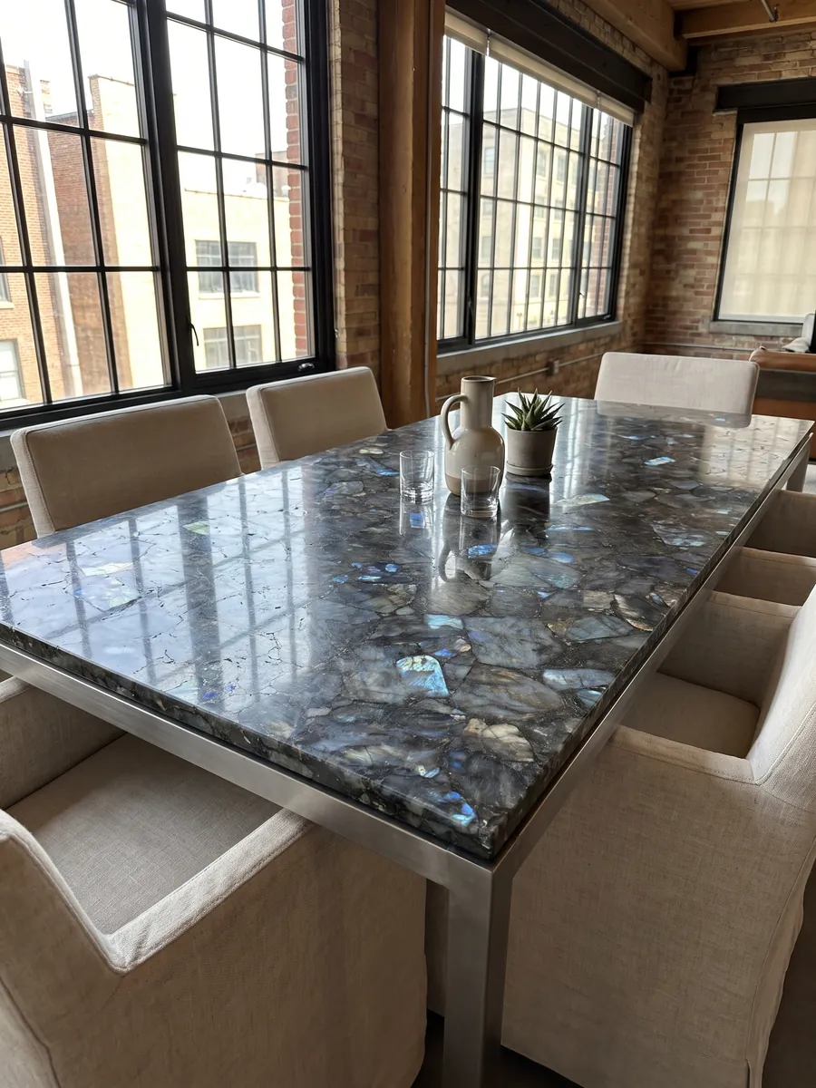 Mesa de comedor con cubierta de Labradorita sobre base de acero: piezas gris oscuro con destellos azules iridiscentes repartidos
