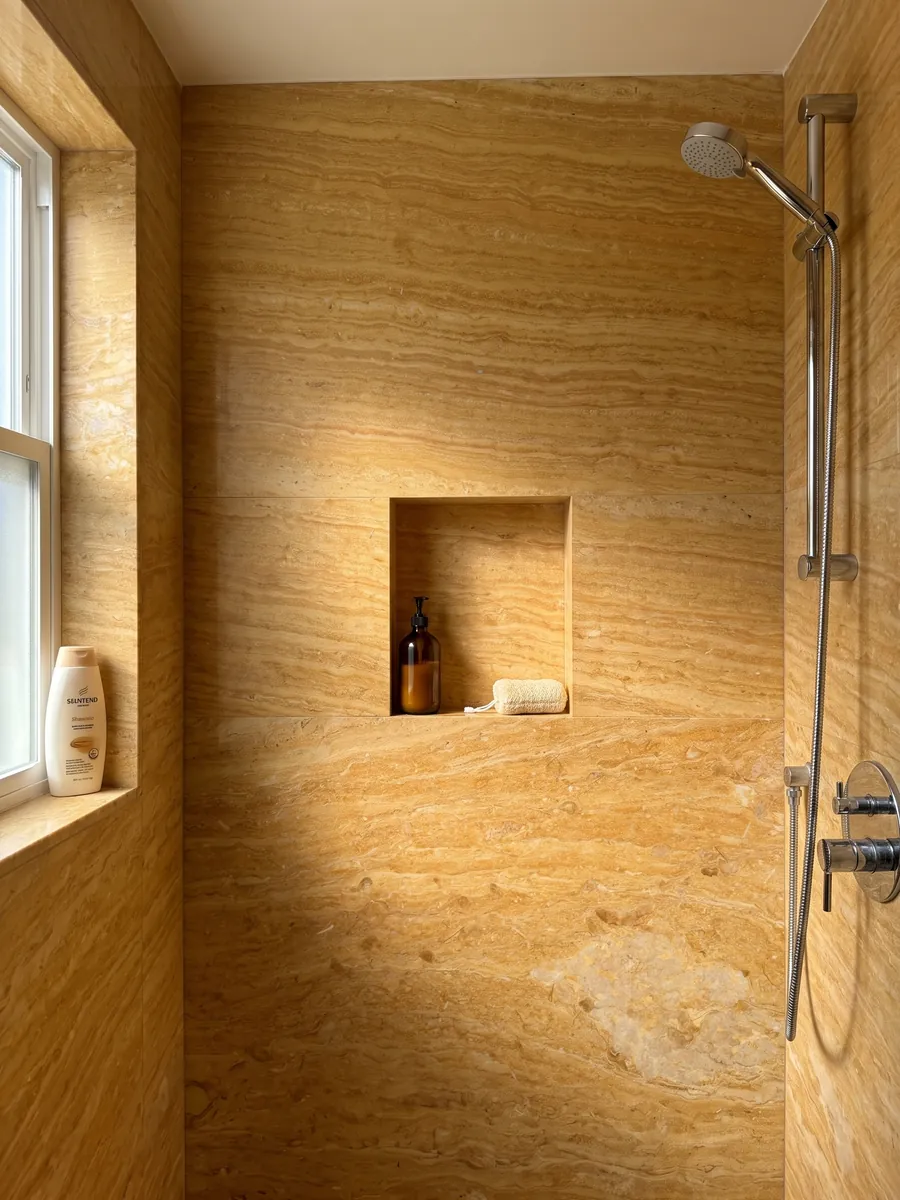 Ducha revestida con placas enteras de Mármol Amarillo Real con nicho empotrado: amarillo ocre intenso con bandas horizontales finas y una zona beige clara abajo a la derecha